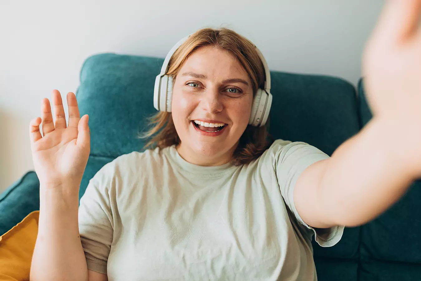 A woman smiling and has her headphones on while waving her hand.