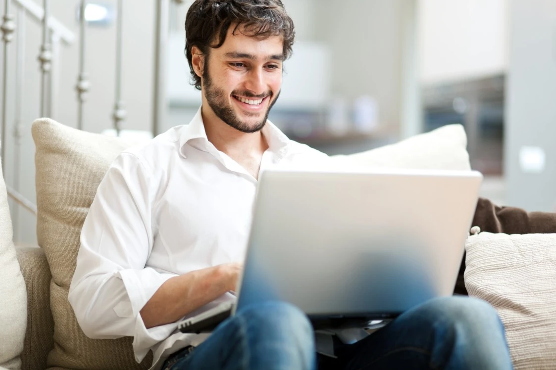 A man smiling while typing on his laptop